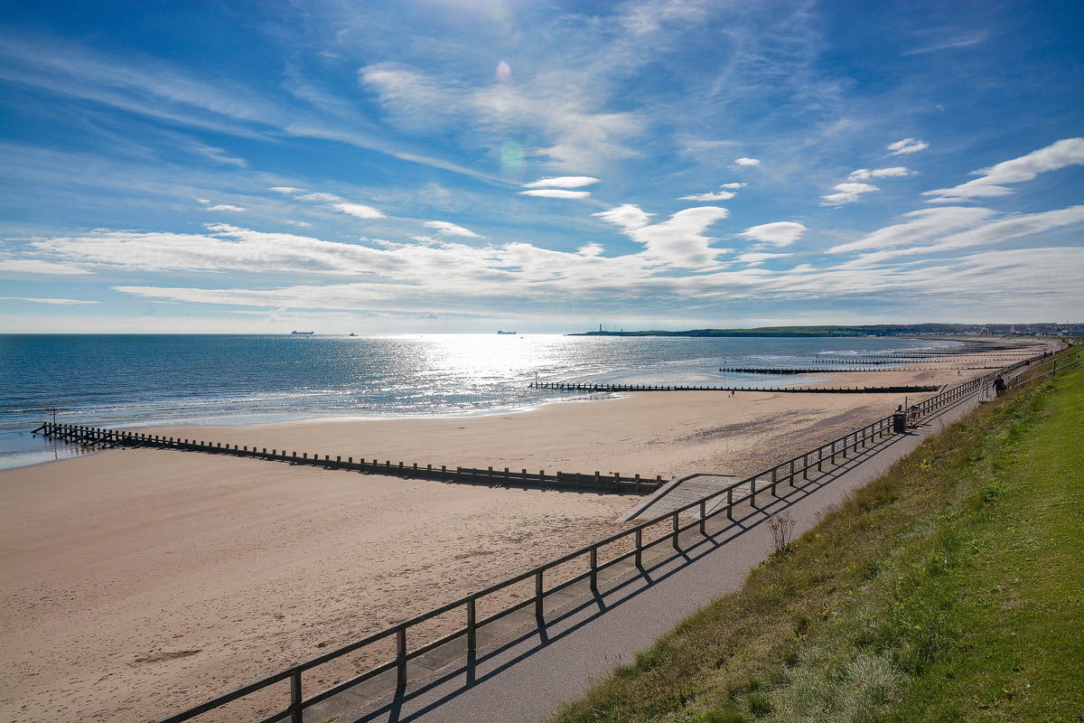Aberdeen Beach looking south from the esplanade with sun reflecting on the calm North Sea and wooden groynes stretching into the distance