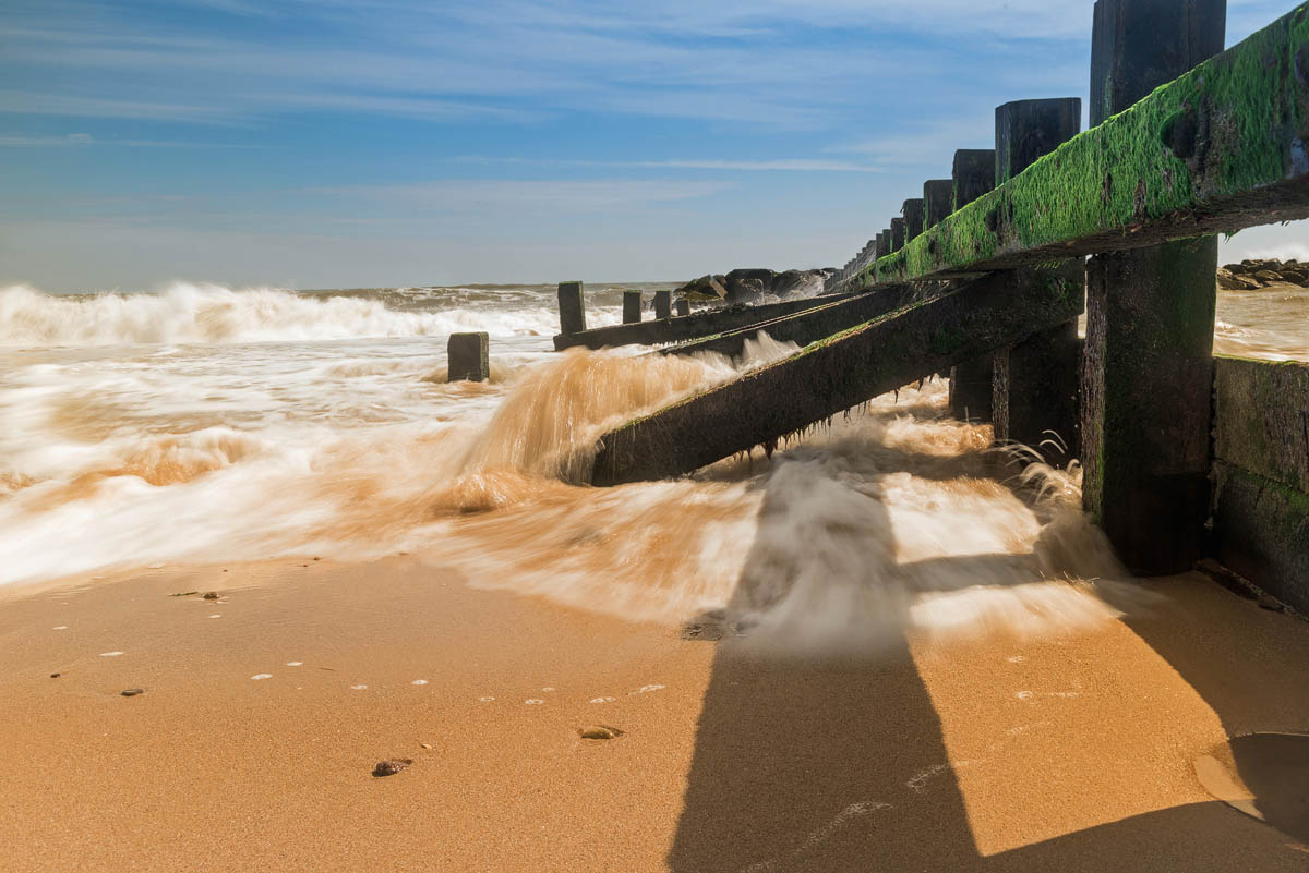 Waves crashing through an algae-covered wooden groyne on Aberdeen Beach