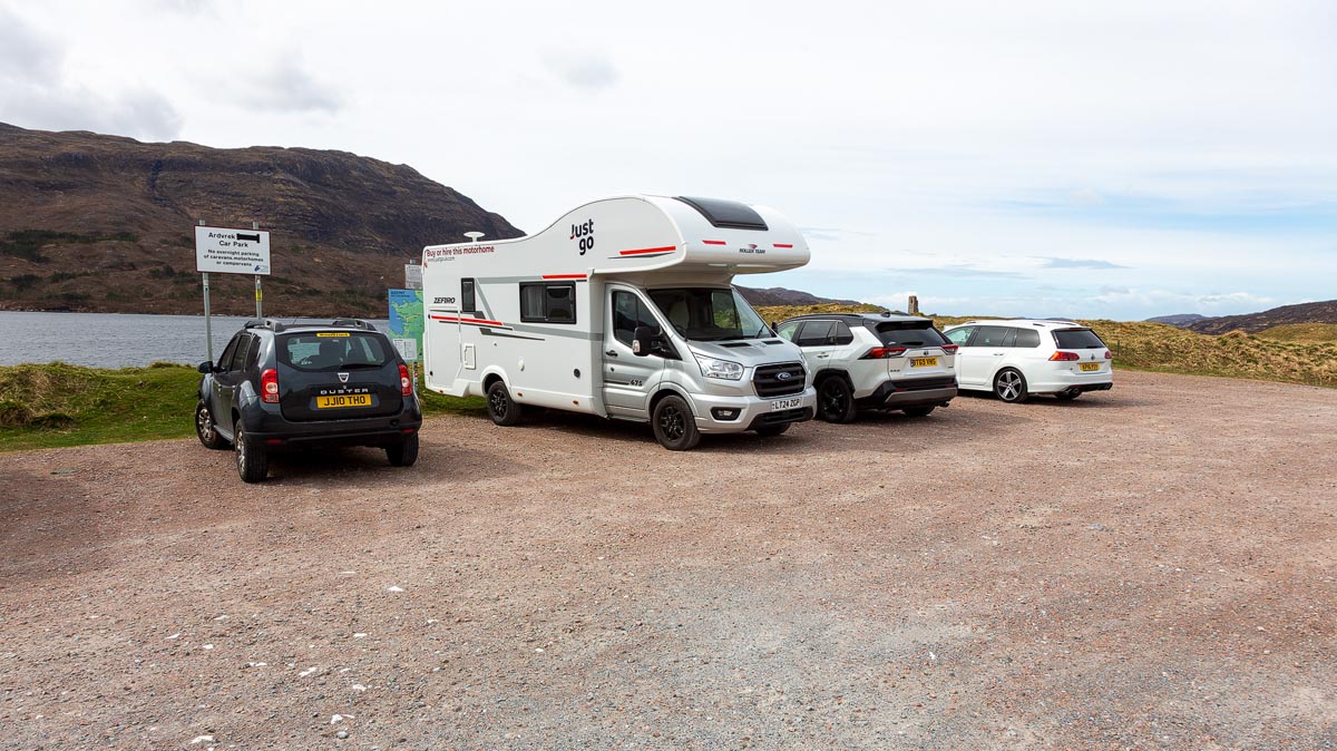 The Ardvreck Castle car park beside Loch Assynt with vehicles and an information sign