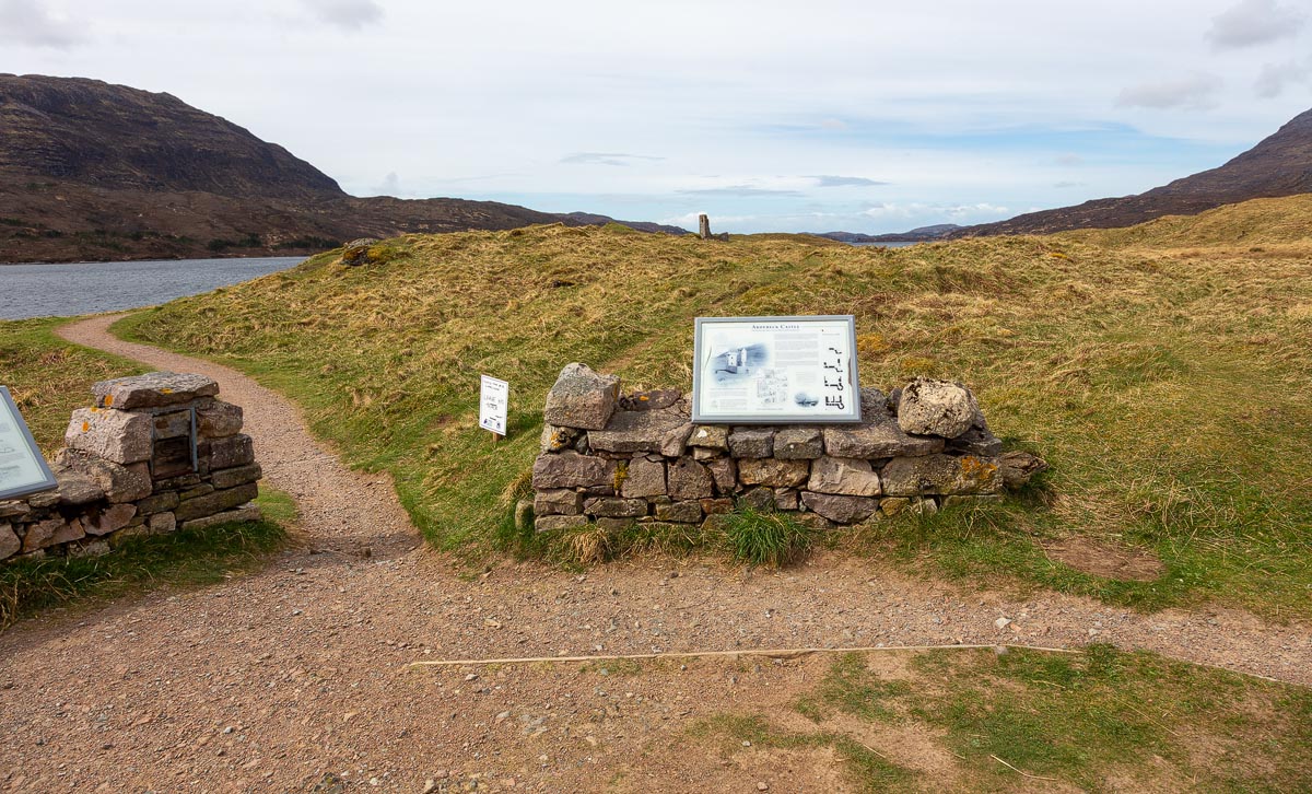 The footpath leading to Ardvreck Castle with an information board and the castle ruins visible on the promontory ahead