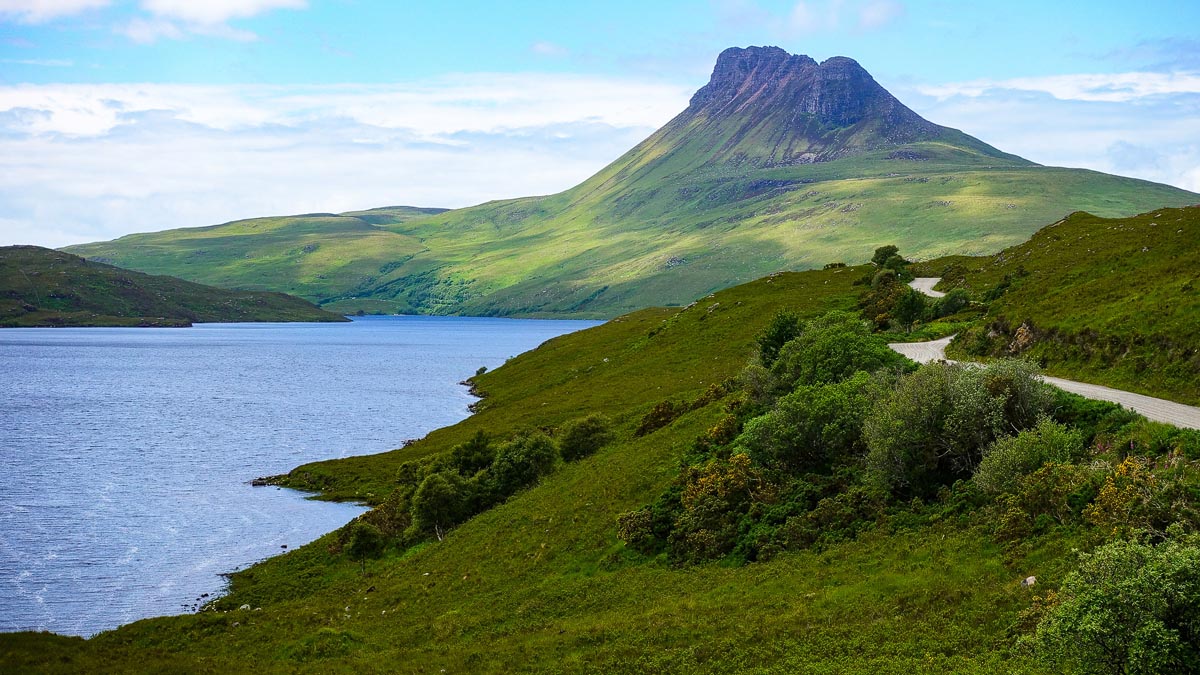 Stac Pollaidh mountain in Assynt viewed across Loch Lurgainn with its distinctive jagged summit profile and a single-track road visible on the hillside