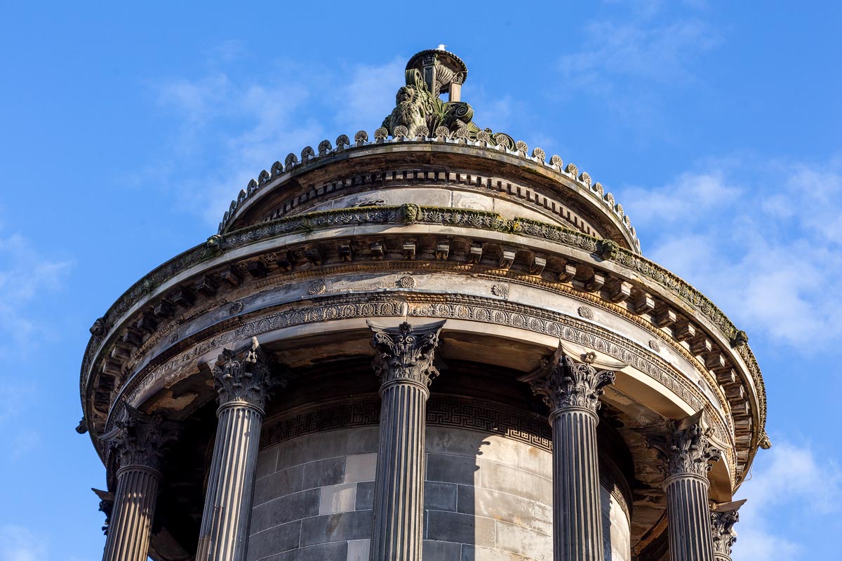 Close-up detail of the Burns Monument dome showing the griffon sculptures, Corinthian column capitals, Greek key frieze, and ornate carved cornice