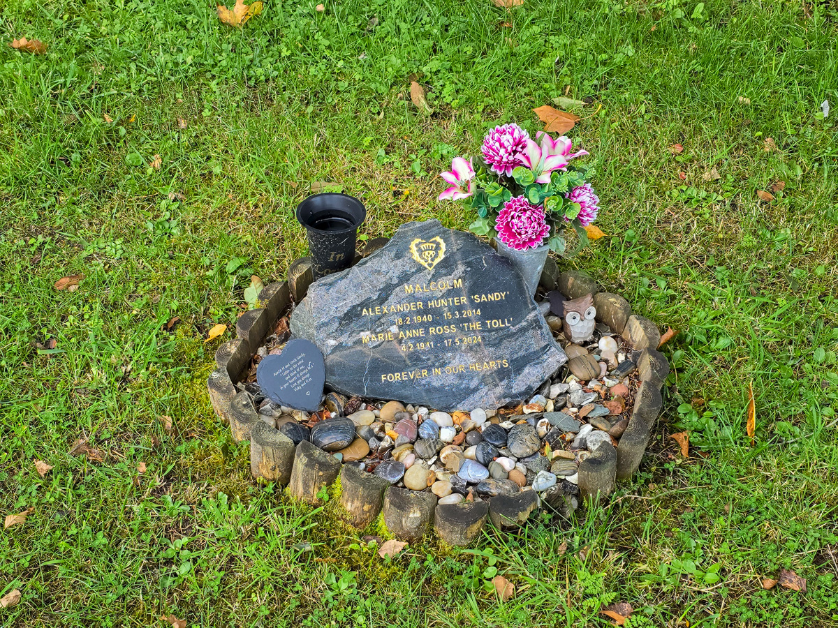 Memorial stone with flowers and pebbles ringed by wooden edging at Califer Hill