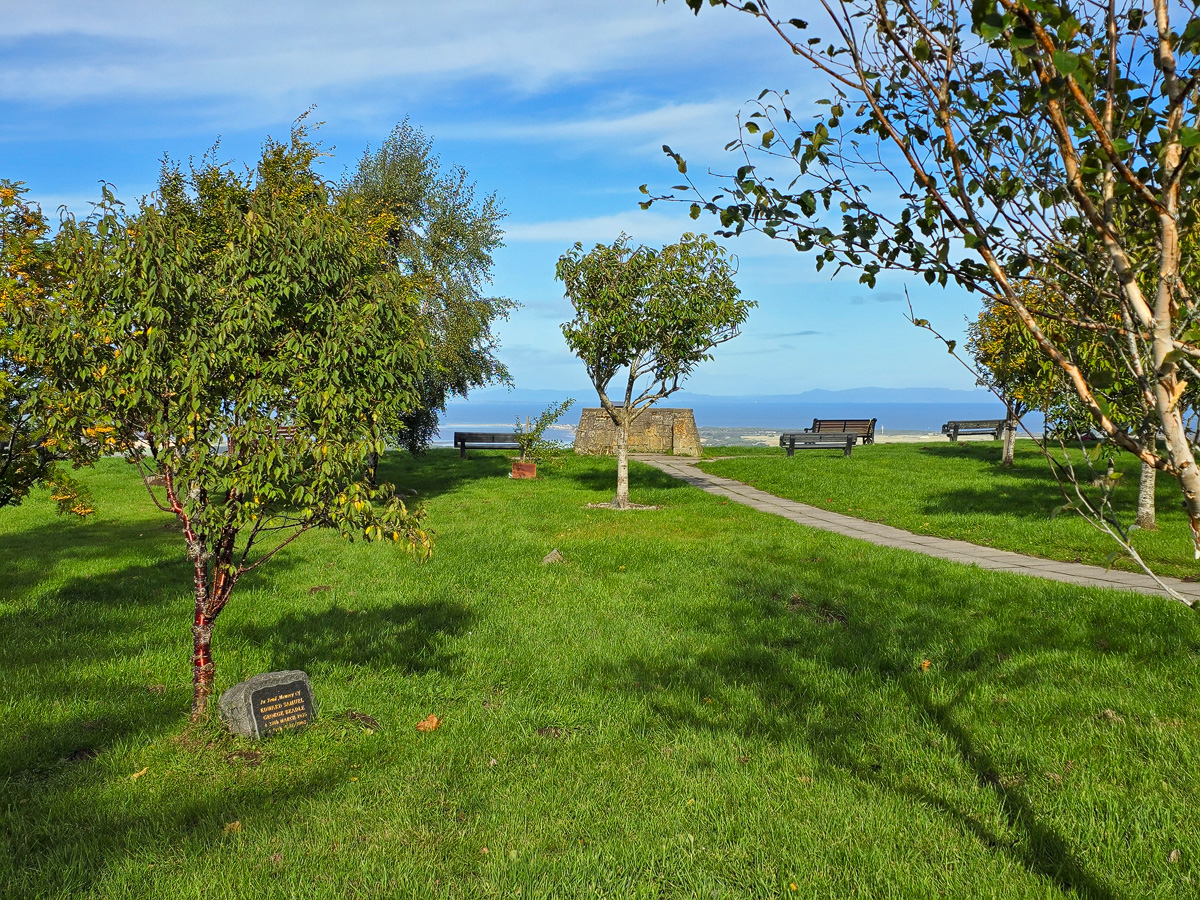 Memorial trees and a stone plaque in front of the viewfinder with the Moray Firth beyond