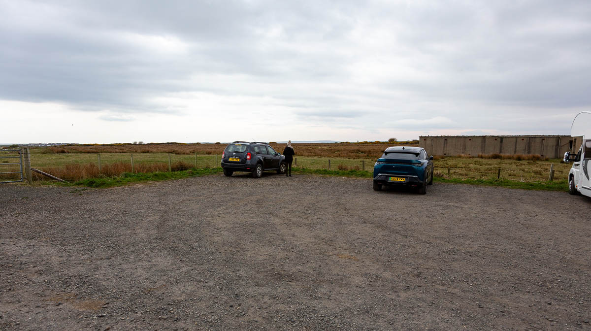 The gravelled car park at Noss Head with vehicles parked and open moorland beyond