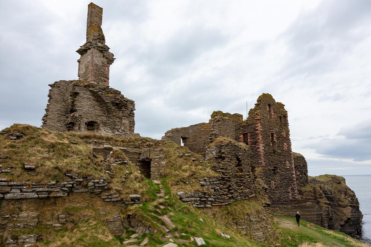 View looking east along the castle promontory showing the chimney stack remnant and the tower house with a visitor for scale