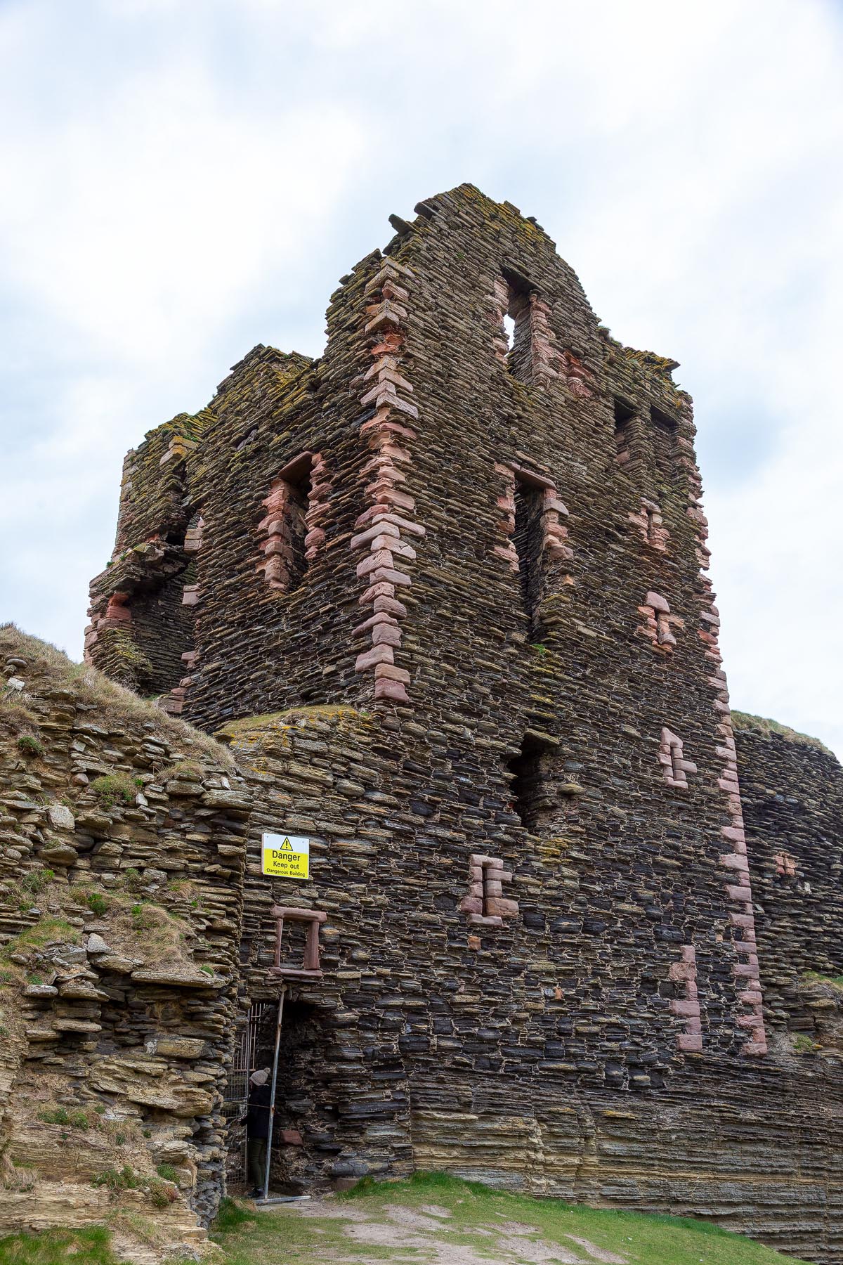Looking up at the tower house of Castle Sinclair Girnigoe showing window openings with red sandstone dressings and a danger warning sign