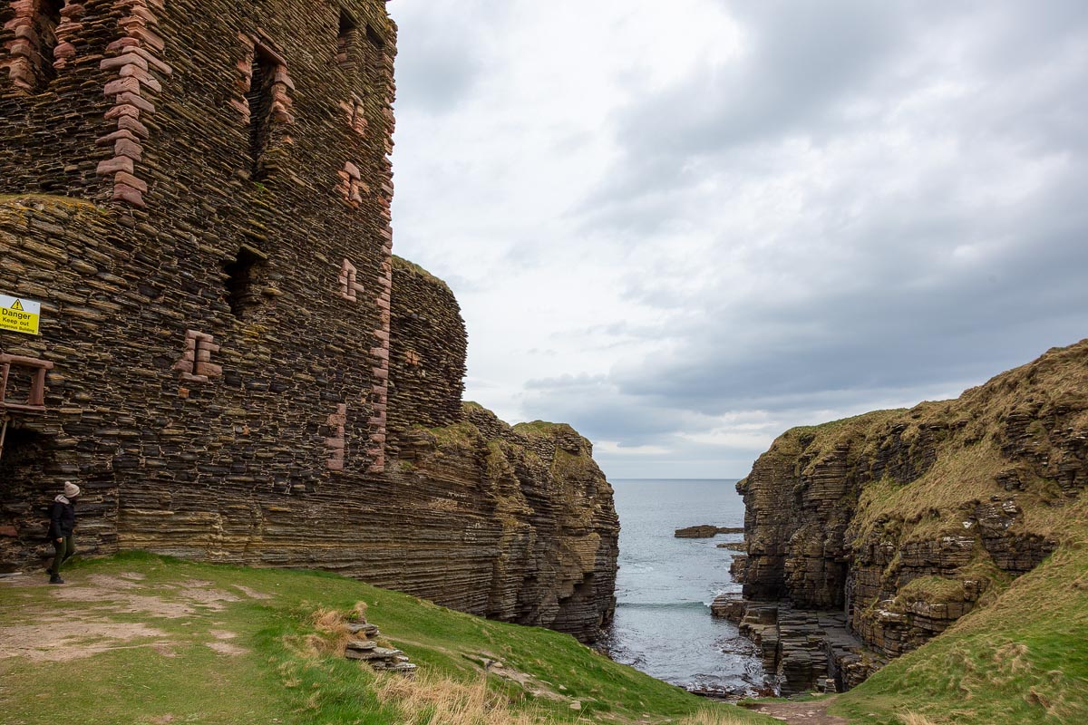View from beside the tower house looking out through a narrow geo to the sea with layered sandstone cliffs on either side