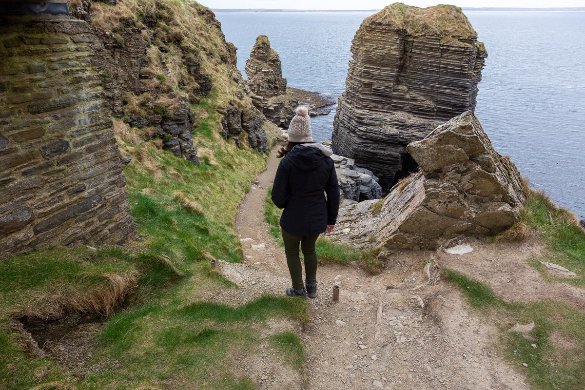 Visitor walking along the narrow coastal path below Castle Sinclair Girnigoe towards sea stacks and the coastline
