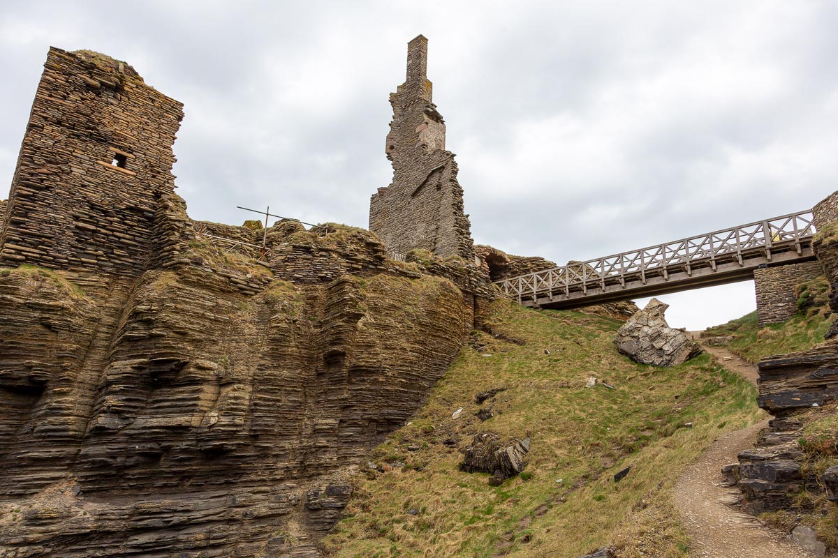 View from below the castle looking up at the ruins and footbridge spanning the rock-cut ditch with the chimney stack rising above