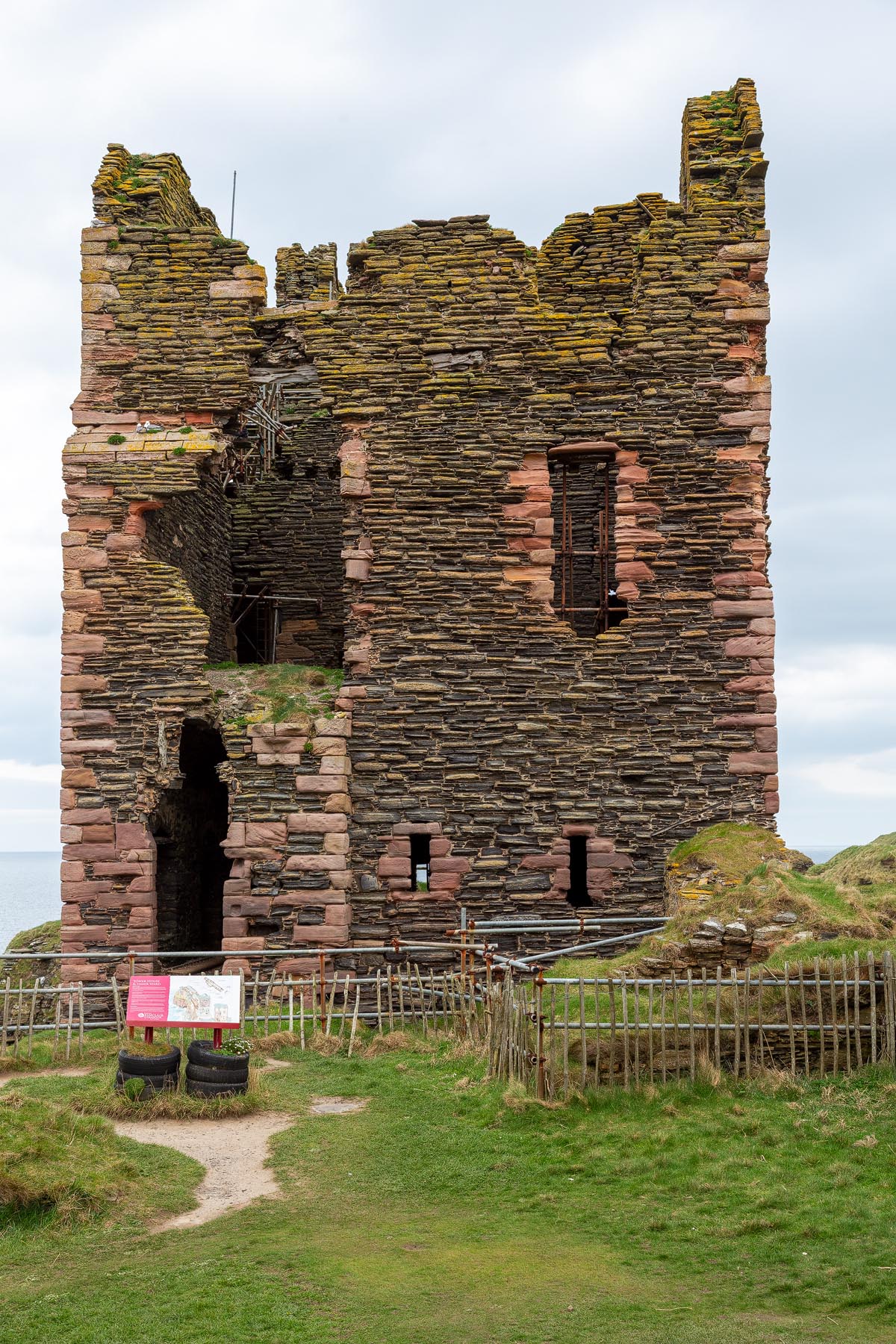 The imposing tower house of Castle Sinclair Girnigoe built from Caithness flagstone and red sandstone, with an information board and safety fencing at its base