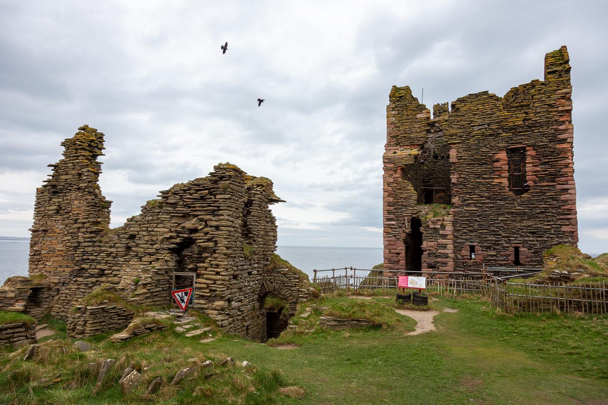 Wider view of the castle courtyard showing ruined walls of the older castle buildings and the tower house with birds circling overhead