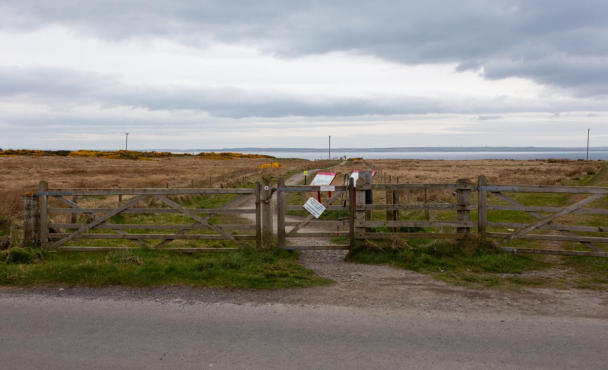 Wooden gate at the start of the walking path to Castle Sinclair Girnigoe with the sea visible in the distance