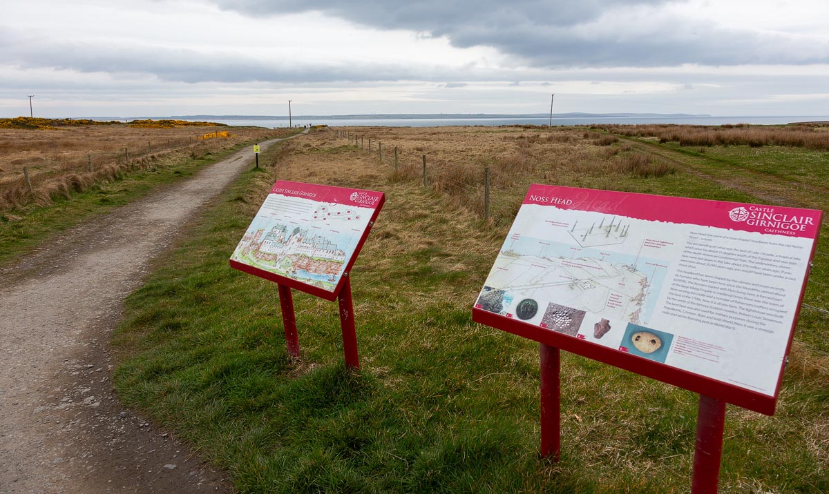Information boards on red frames beside the coastal path showing castle history and Noss Head natural heritage