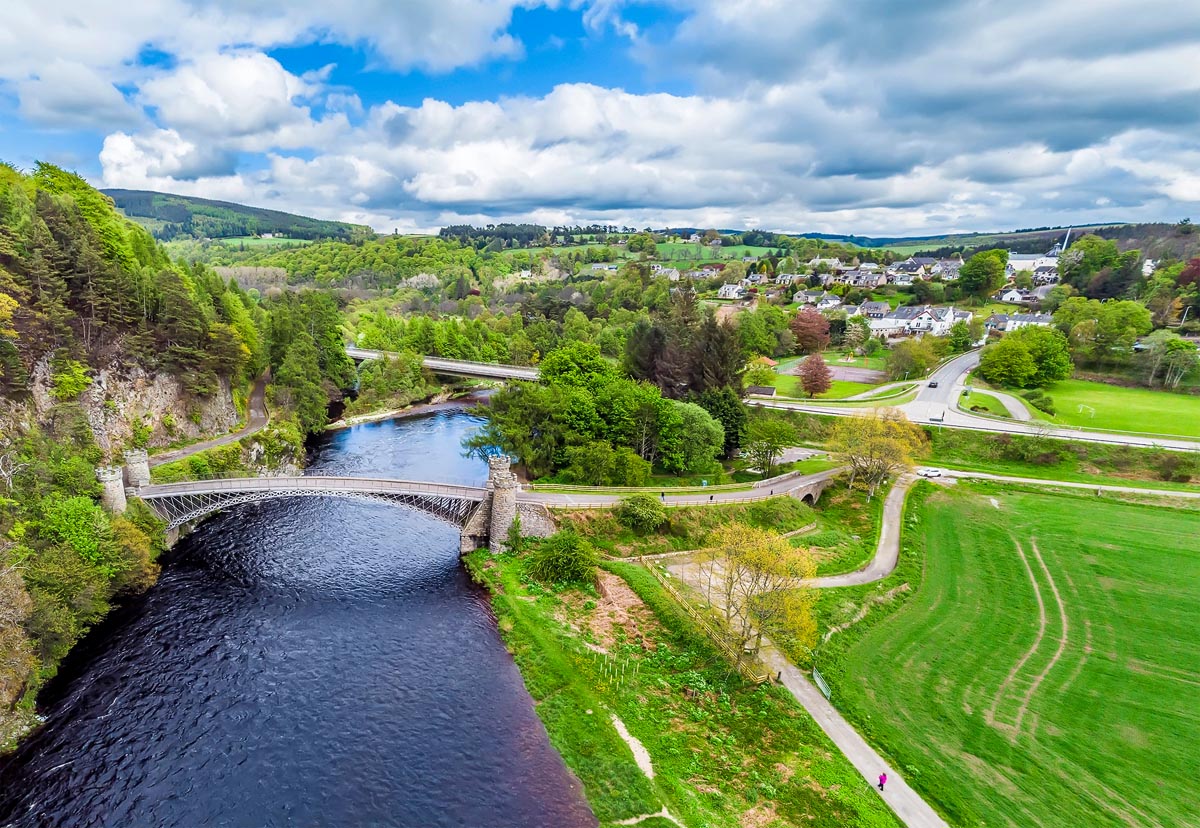 Aerial view of the historic Craigellachie Bridge spanning the River Spey with the village and green hills beyond