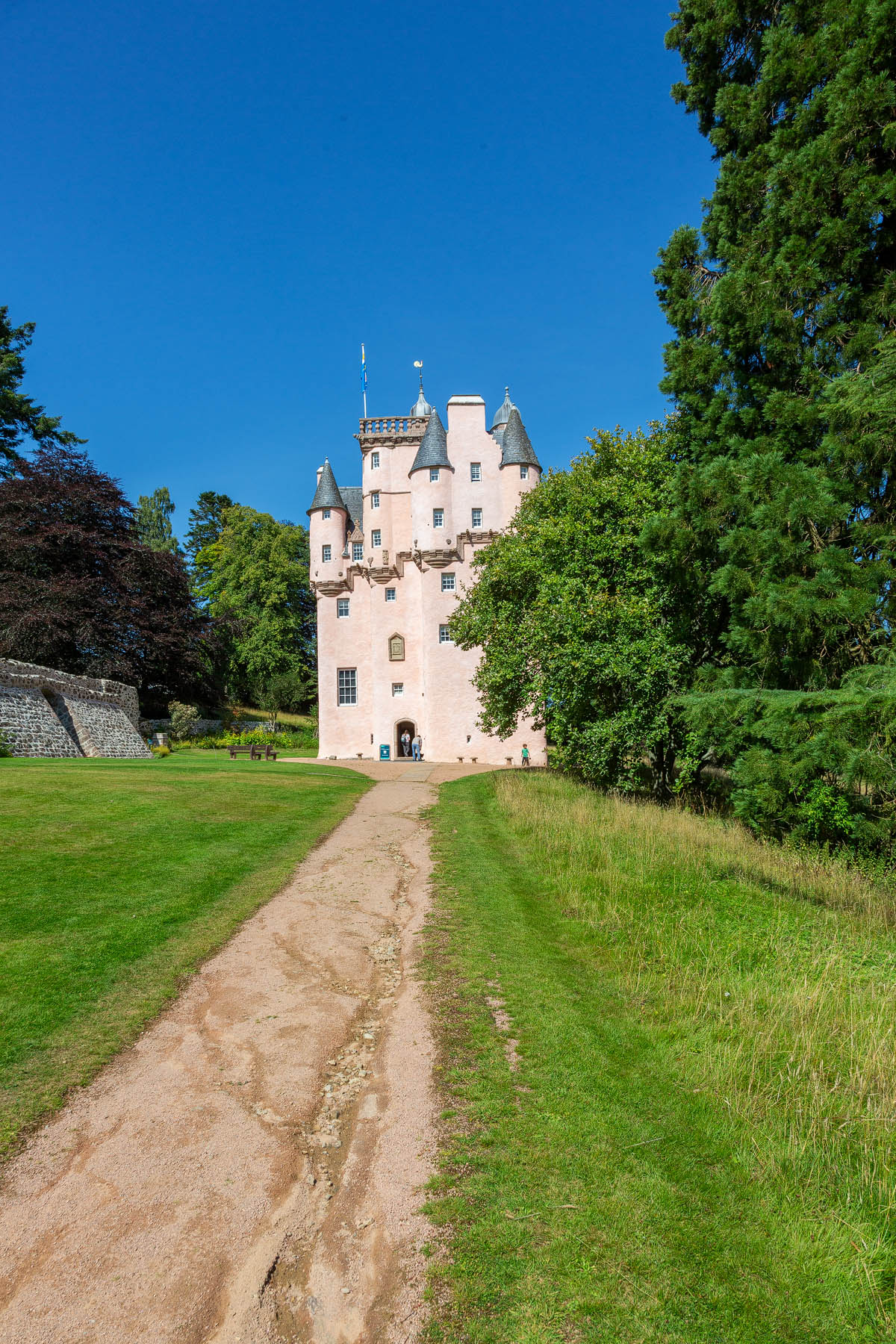 The path leading to the entrance of Craigievar Castle showing the full seven-storey height of the pink tower against a clear blue sky