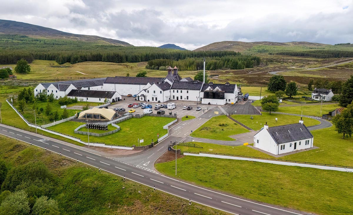 Aerial view of Dalwhinnie Distillery showing the white-painted buildings with twin pagodas set against Highland moorland and hills