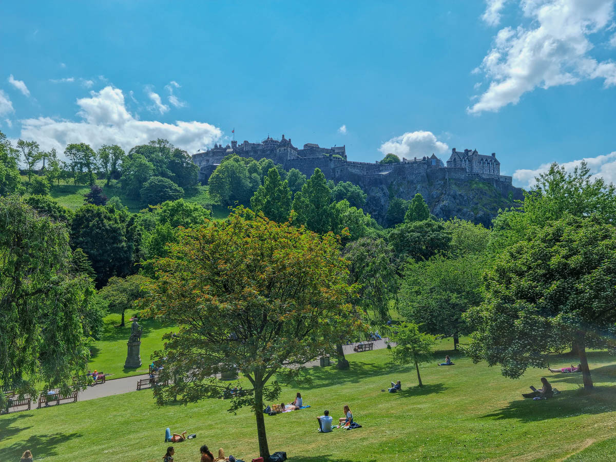 Edinburgh Castle rising above the lush green trees of Princes Street Gardens on a sunny summer afternoon