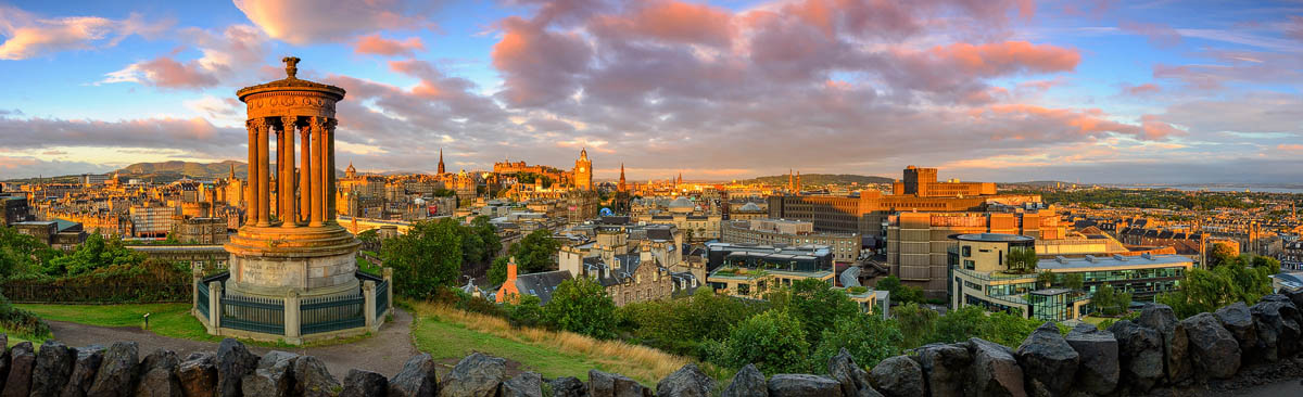 Panoramic sunset view from Calton Hill showing the Dugald Stewart Monument and Edinburgh's skyline bathed in warm light
