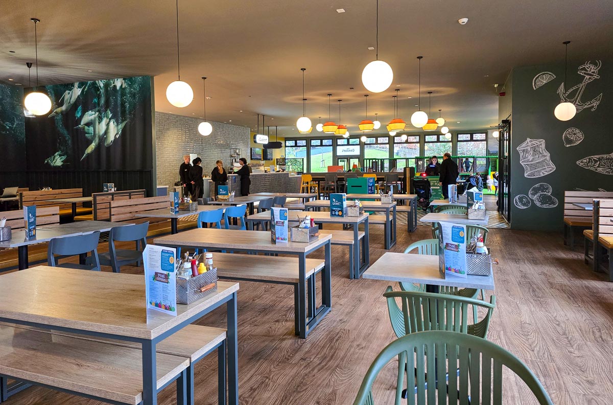 Interior of The Gannet restaurant at Edinburgh Zoo with wooden tables and penguin underwater mural
