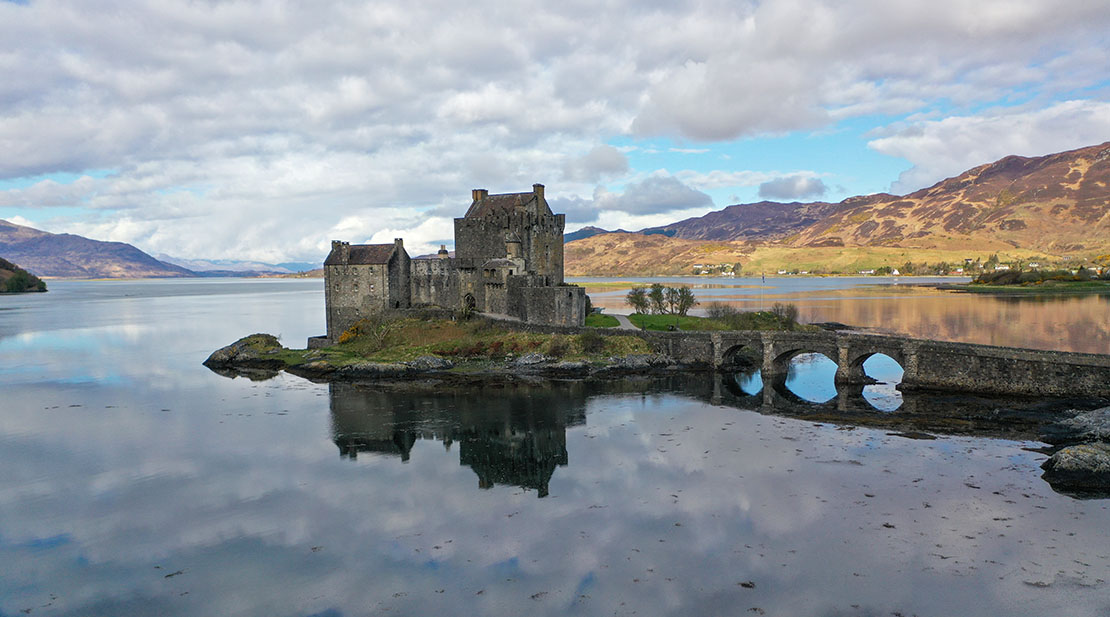 The iconic view of Eilean Donan Castle with its arched stone footbridge reflected in a glass-calm loch