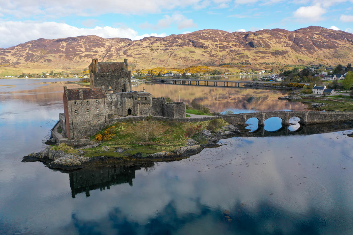 Eilean Donan Castle from the air with the footbridge and the village of Dornie visible across the loch in the distance