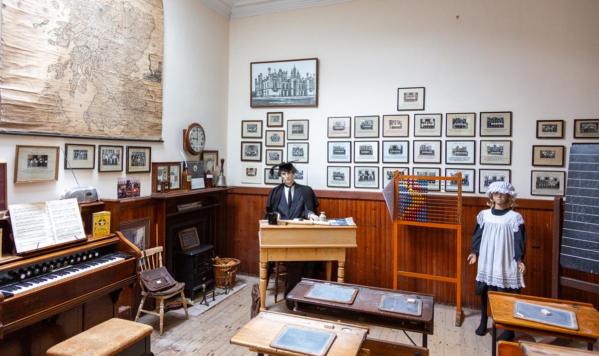 The recreated Milne's Free School classroom with mannequin teacher, pupil, period desks, and school photographs