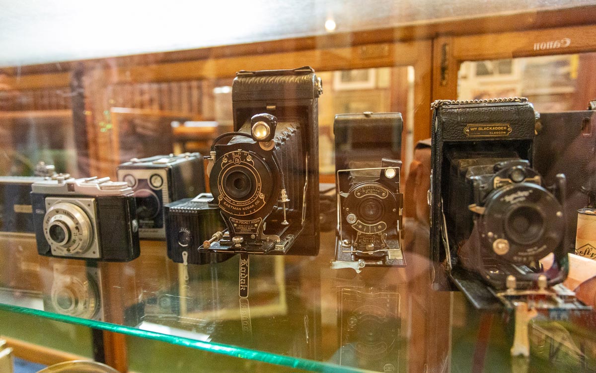 A collection of vintage cameras including Eastman Kodak and Ensign models displayed in a glass case