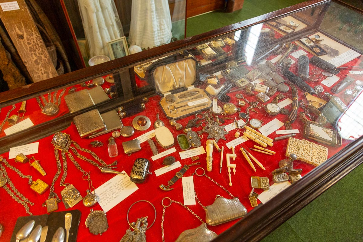 A glass display case lined with red velvet containing vintage pocket watches, jewellery, cigarette cases, and personal accessories