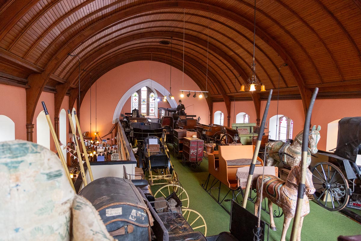 The upper gallery of Fochabers Folk Museum filled with horse-drawn carriages beneath the barrel-vaulted wooden ceiling