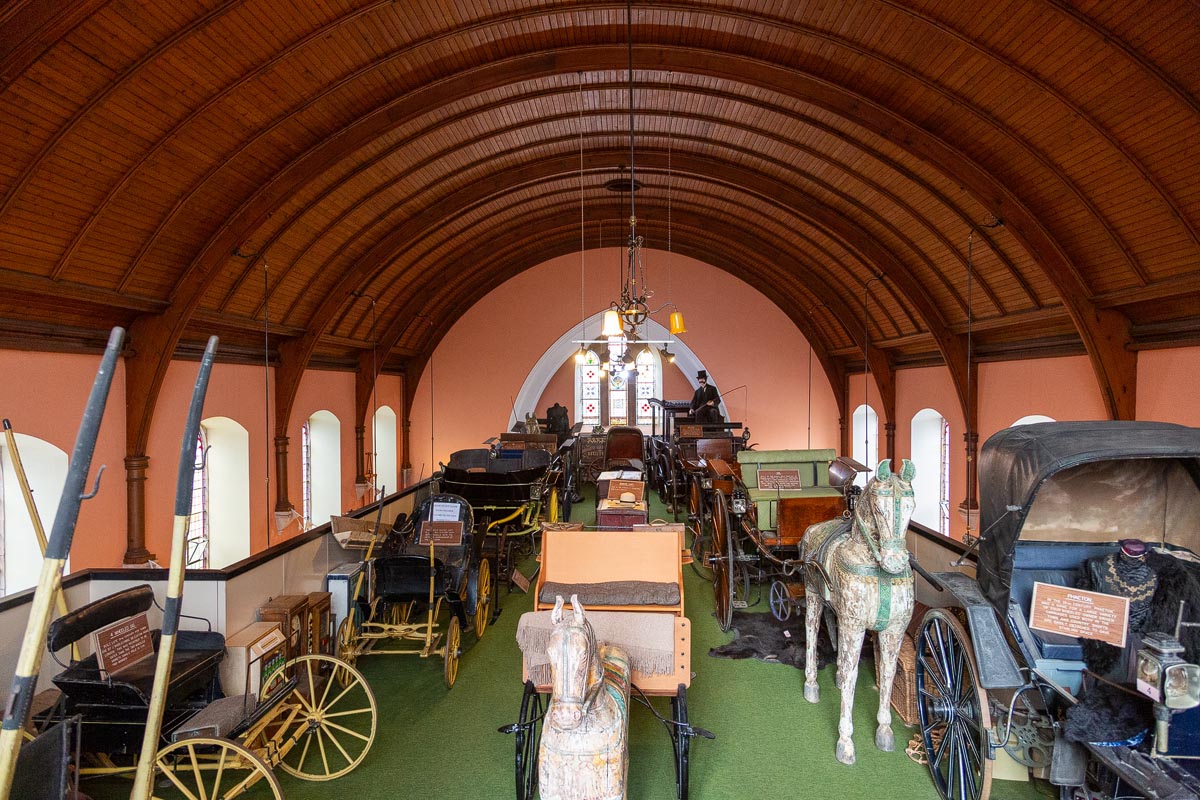A wide view of the upper gallery showing the extensive carriage collection, wooden rocking horses, and the vaulted ceiling