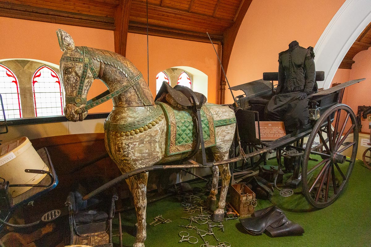 A carved wooden horse and mannequin coachman with a carriage on the upper floor of the museum
