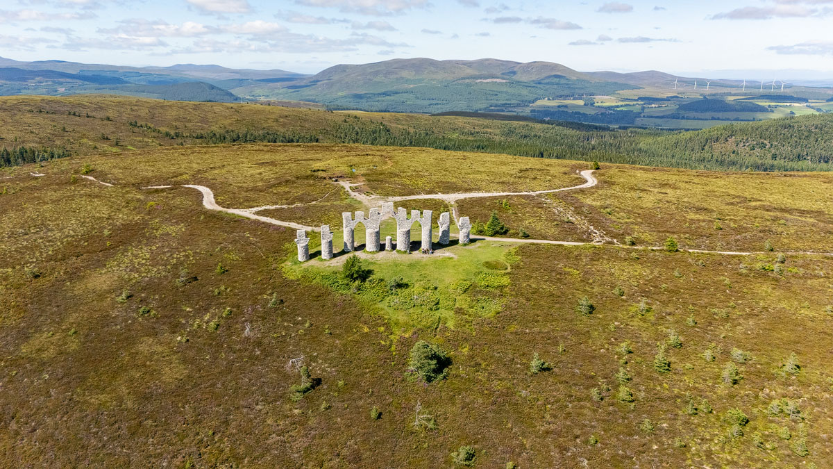 High wide drone shot showing the Fyrish Monument small amid the vast moorland plateau with hills and a wind farm on the horizon