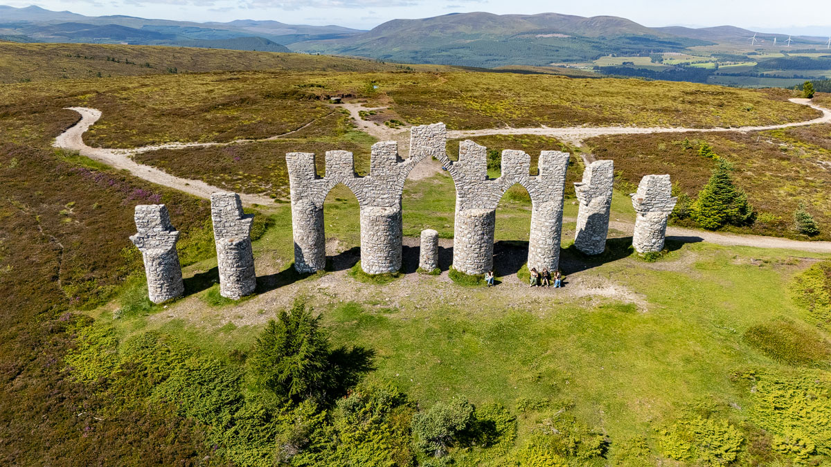 Low drone shot face-on to the Fyrish Monument with the family sitting at its base and hills behind