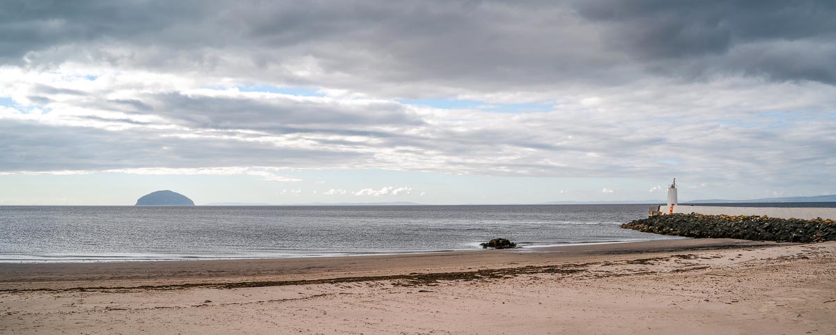 Girvan Beach with golden sand, Ailsa Craig island on the horizon, and a small lighthouse on the breakwater