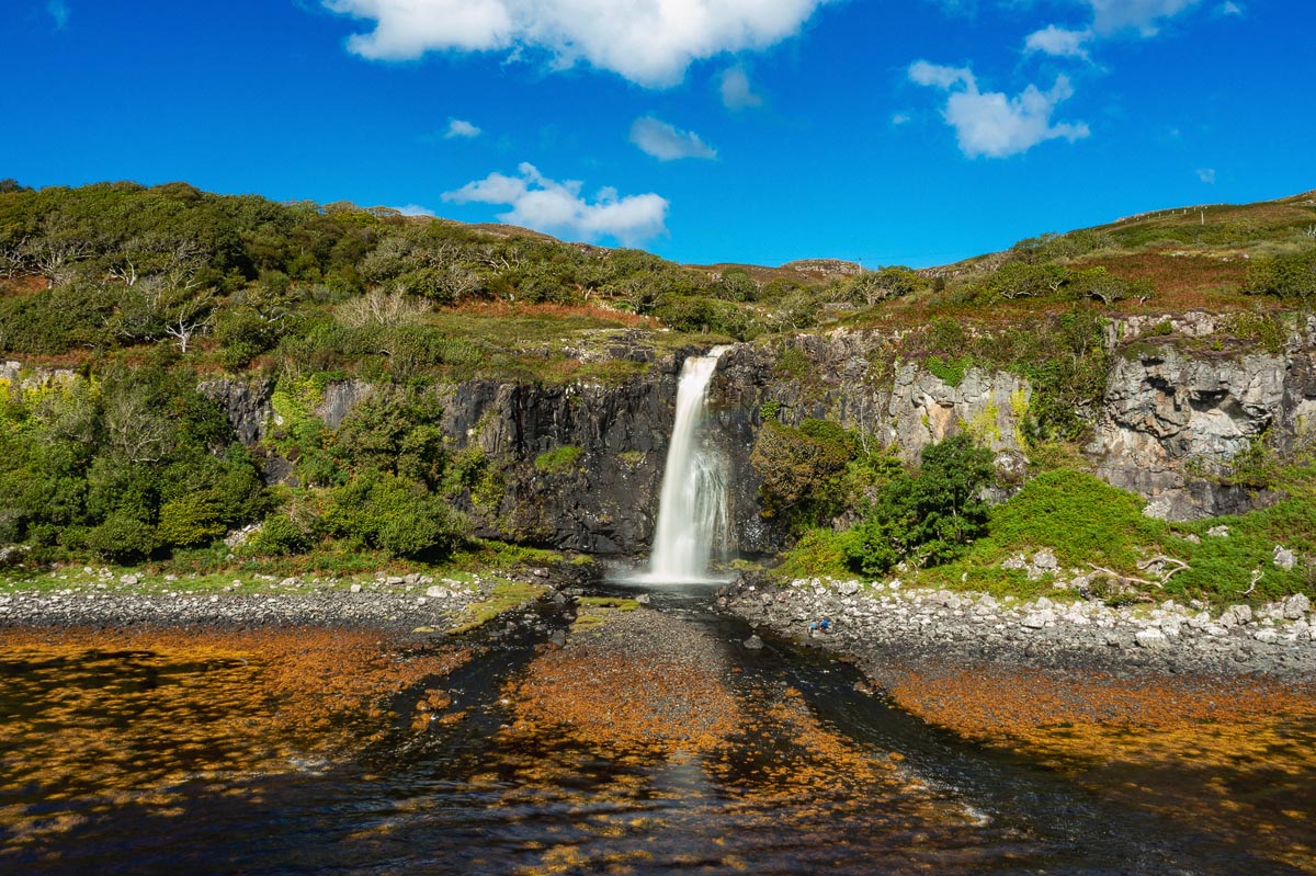 Eas Fors waterfall on the Isle of Mull dropping over a cliff face into a rocky shoreline pool
