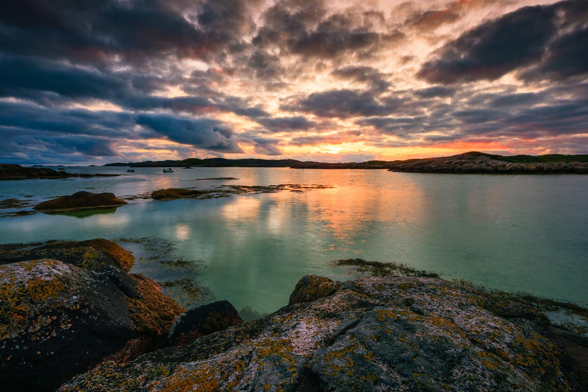 A dramatic sunset over the rocky coastline of the Ross of Mull with clear turquoise water and lichen-covered rocks