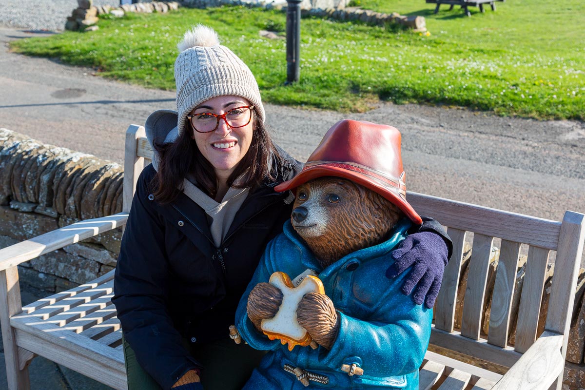 Janette posing with the Paddington Bear statue on the bench at John o' Groats
