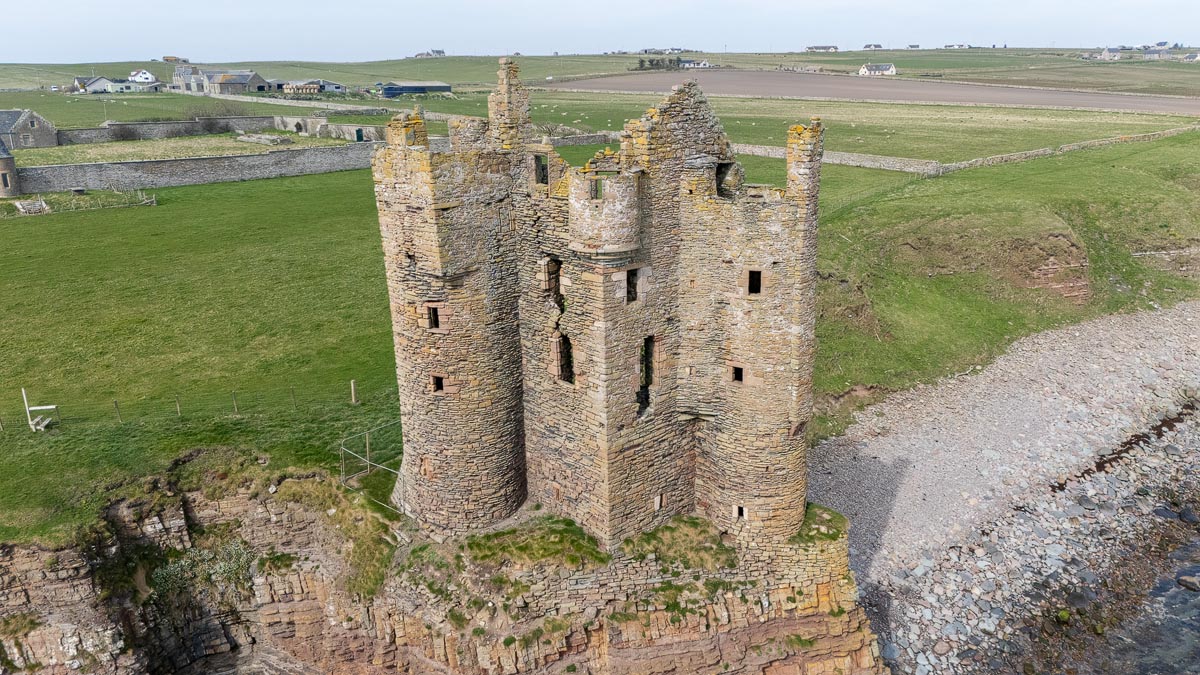 Aerial close-up of Old Keiss Castle showing the two round towers and Z-plan layout with farmland behind