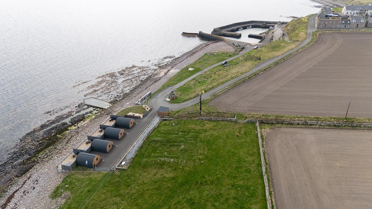 Drone view looking back towards Keiss Harbour showing glamping pods and the road along the coast