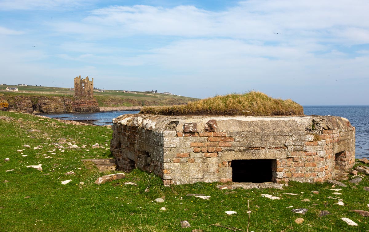 WW2 pillbox in the foreground with Old Keiss Castle ruins visible across the bay in the background