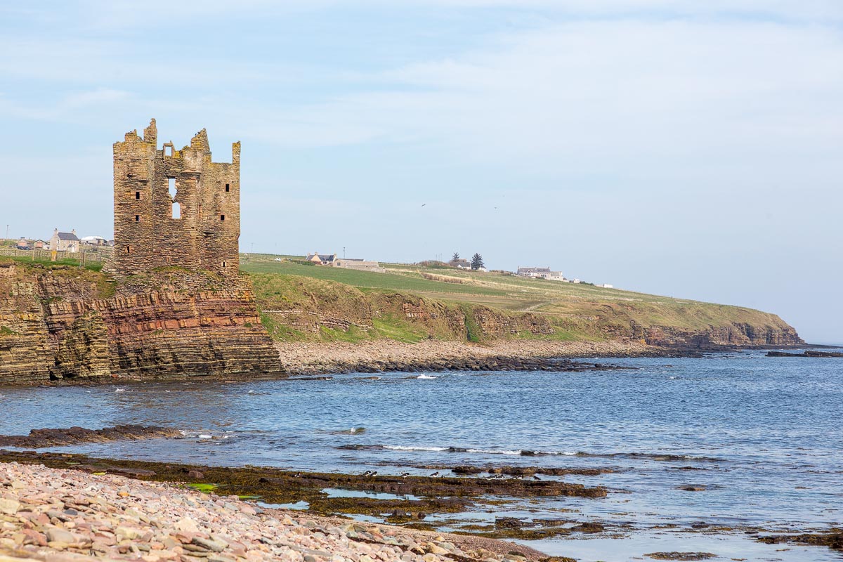 Old Keiss Castle viewed from the rocky shoreline, the tower rising from layered sandstone cliffs