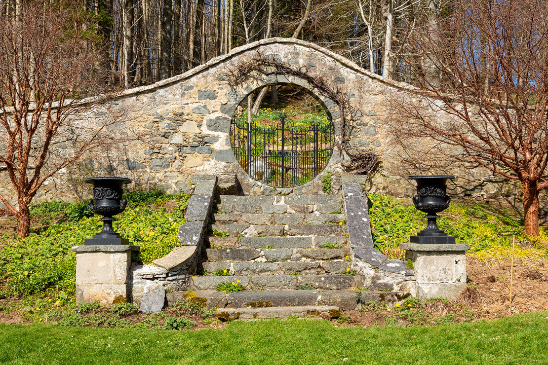 Leith Hall Gardens circular gateway. Moon gate. Steep mountains rise behind.