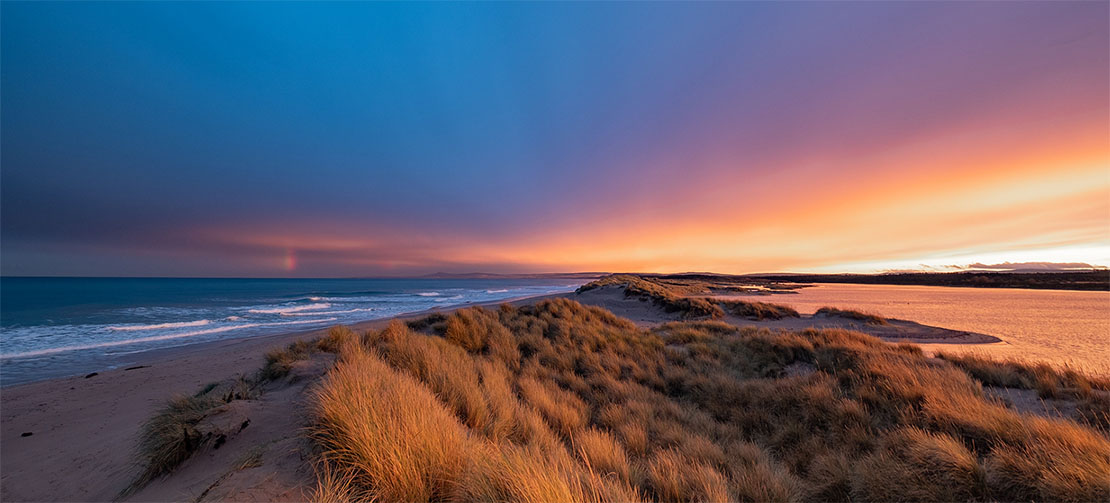 Spectacular sunset over Lossiemouth East Beach with golden dunes, a rainbow, and vivid orange and purple sky