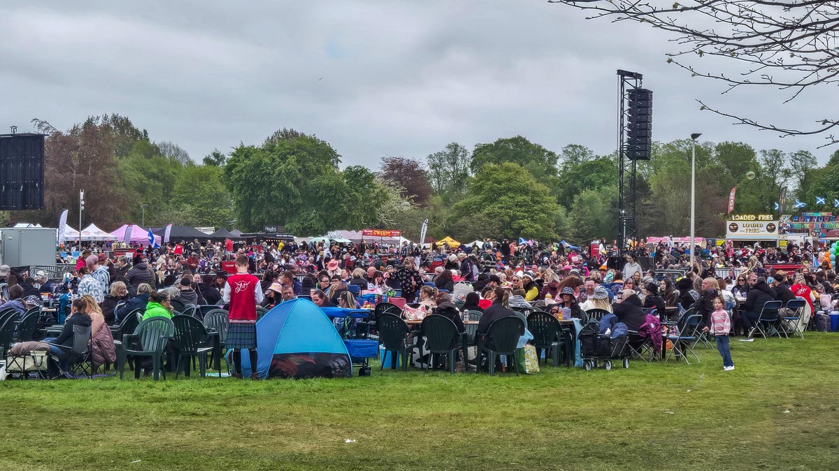 Crowds of festival-goers at tables with Loaded Fries food vendor and PA stack visible behind