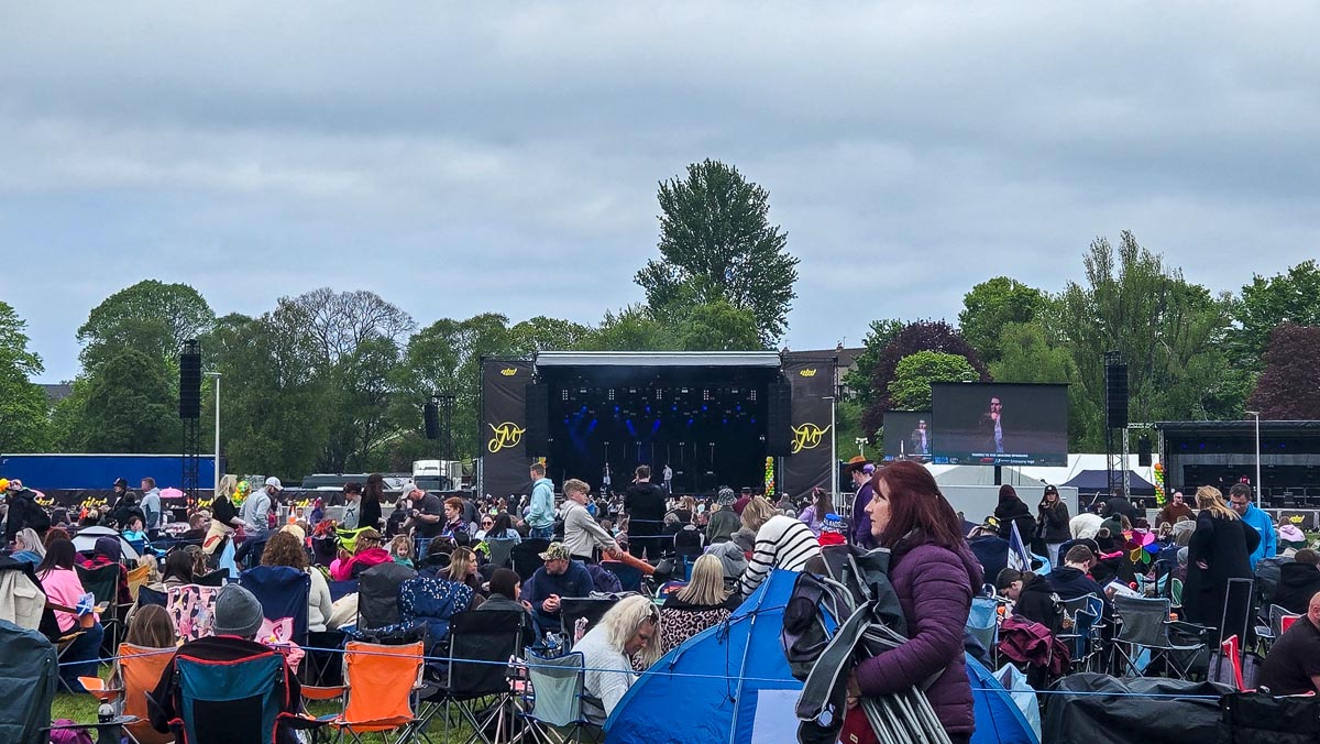 View of MacMoray main stage from middle of crowd with big-screen relay and people in camping chairs and tents