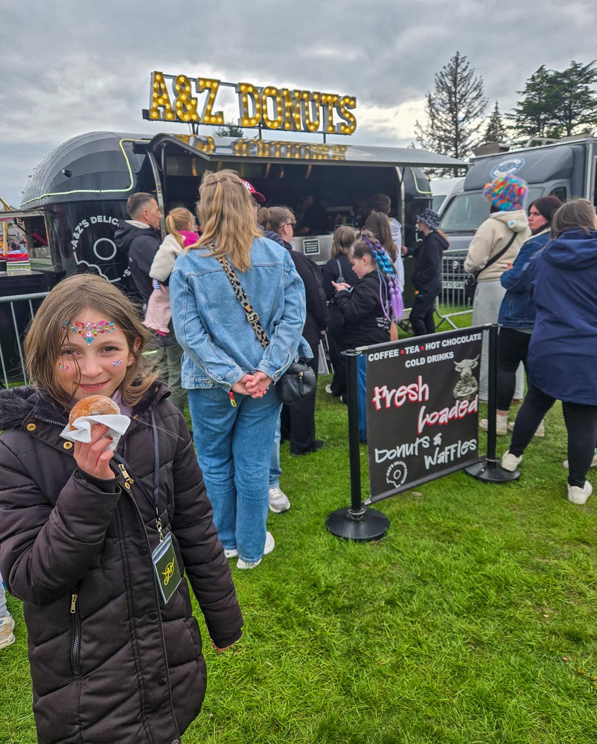 Young girl with face jewels holding a fresh jam donut at the A&Z Donuts trailer at MacMoray