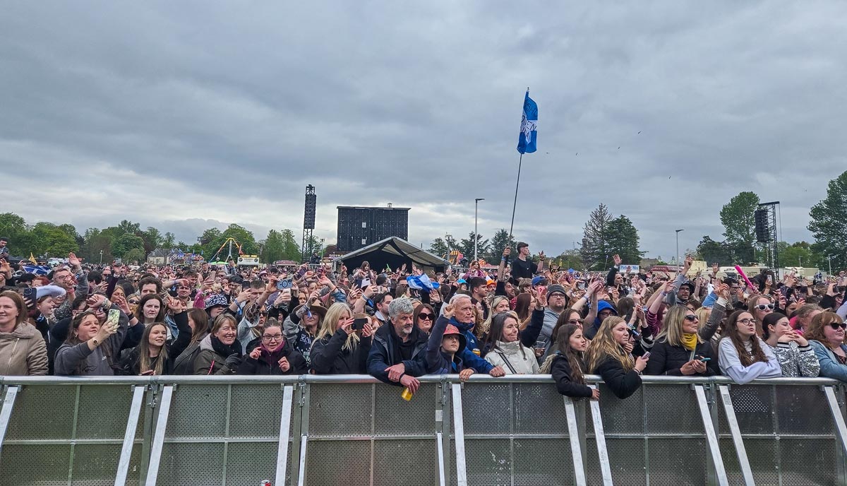 Crowd packed against front barriers at MacMoray main stage with hands raised and a flag flying