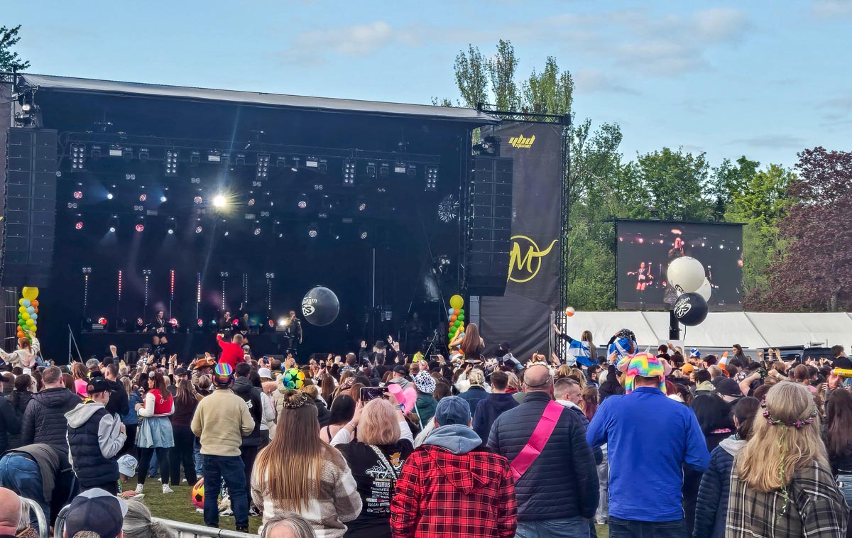 MacMoray main stage at dusk with crowd watching and big-screen relay showing performer