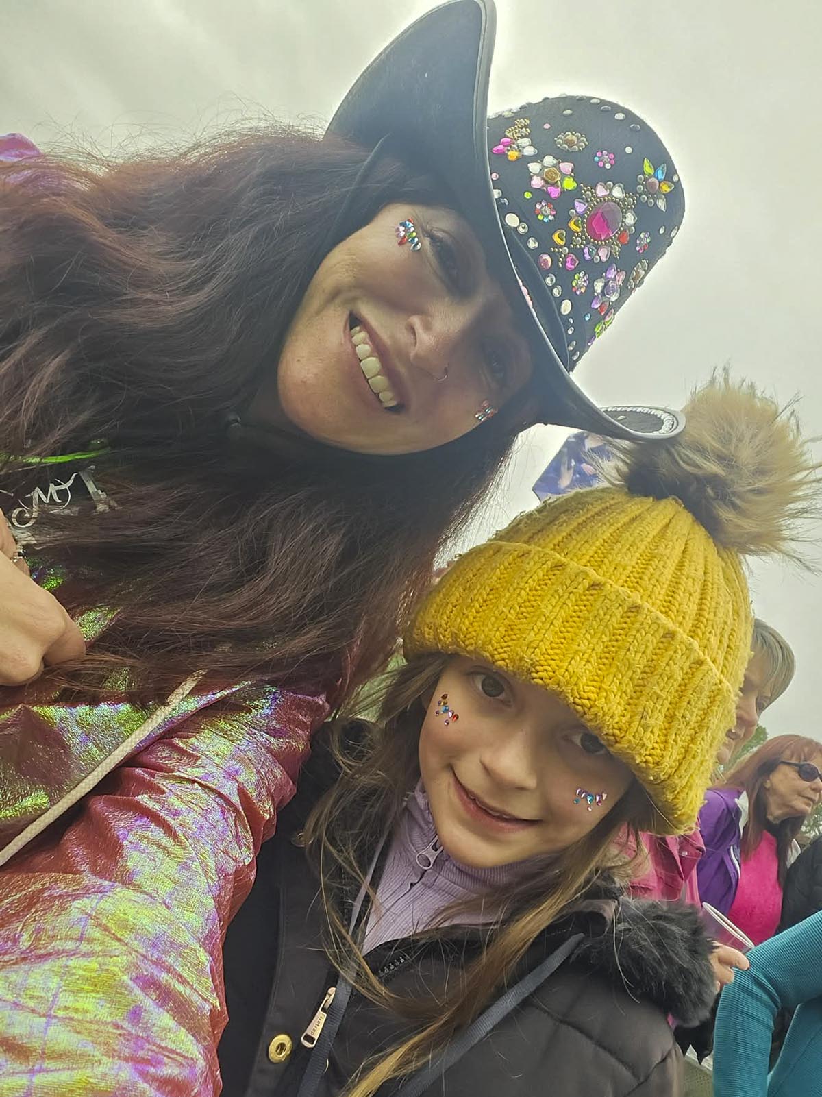 Selfie of Janette in jewelled cowboy hat and iridescent jacket with daughter Lauren in yellow bobble hat